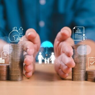 Hands surround stacks of coins with financial icons, a small house, and a piggy bank. Concepts of saving, investment, and protection are depicted.