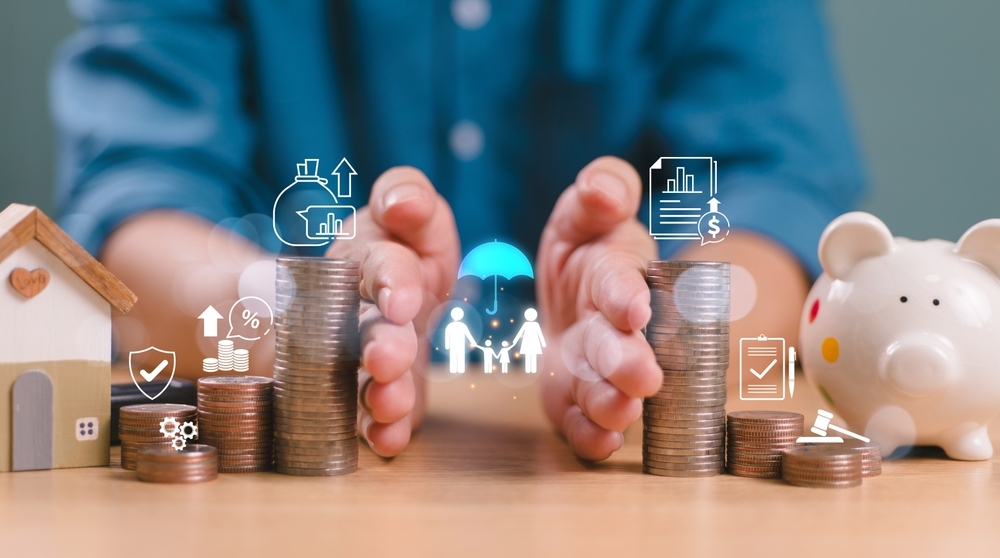 Hands surround stacks of coins with financial icons, a small house, and a piggy bank. Concepts of saving, investment, and protection are depicted.