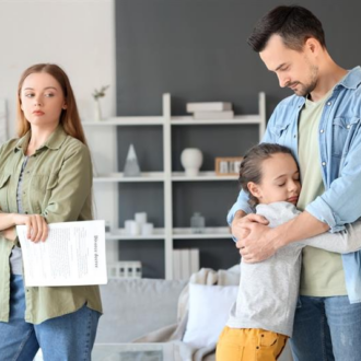 A young girl embraces her father, conveying a sense of comfort, while a woman stands nearby holding divorce papers, looking serious and reflective.
